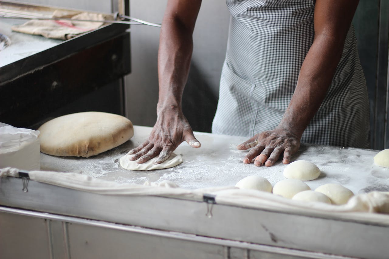 why-choose-us A baker in an indoor kitchen kneading dough for bread preparation, showcasing traditional baking techniques.